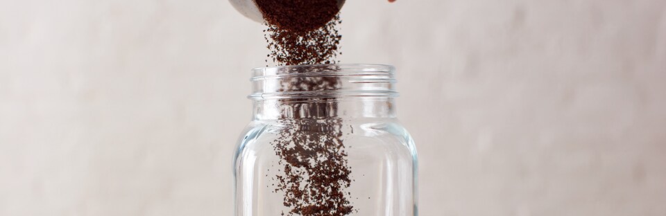 Pouring ground coffee into large glass jar.