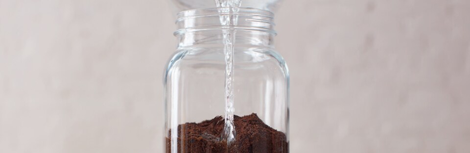 Pouring water over coffee grounds in large glass jar.