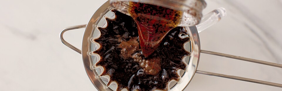 Straining brewed coffee mixture into glass jar.