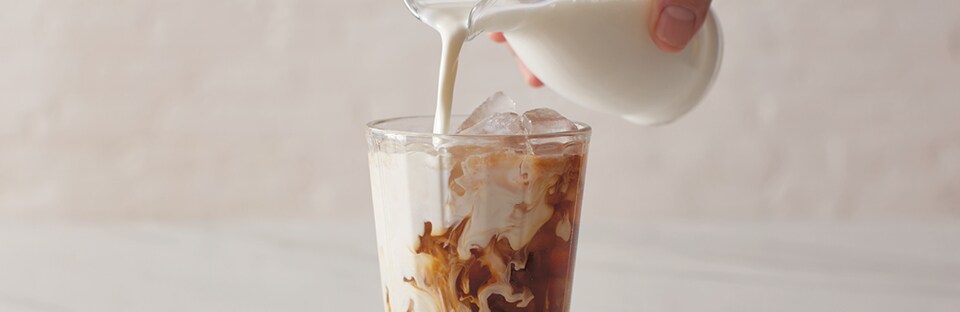 Pouring milk over glass of cold brew coffee.
