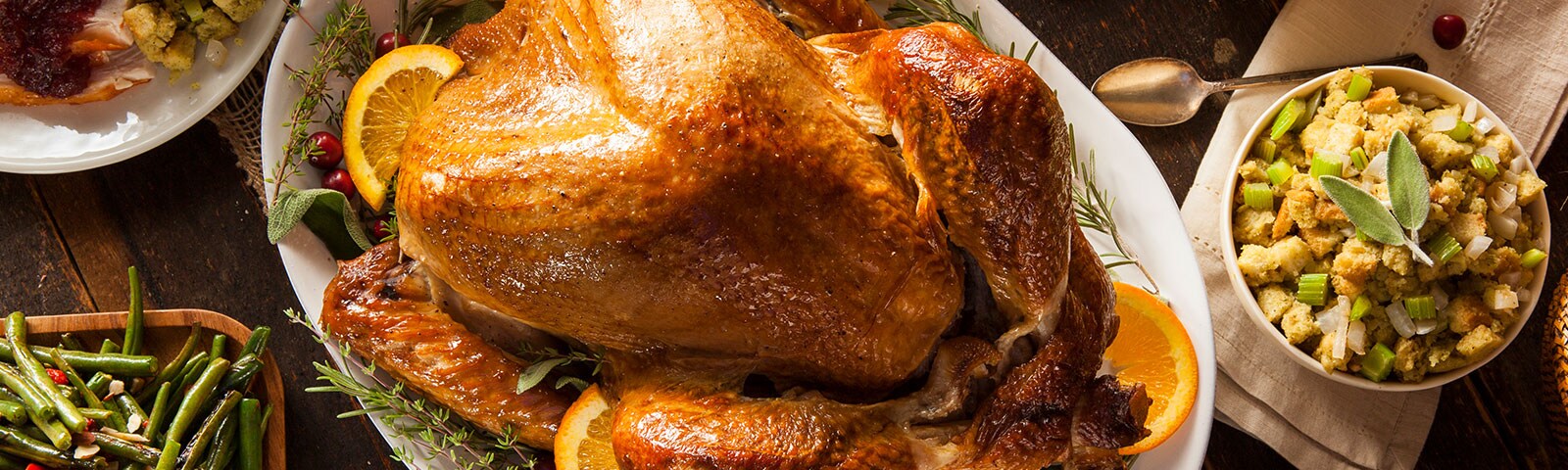 A rustic wooden table covered in various thanksgiving side dishes with a large turkey on a serving plate in the center