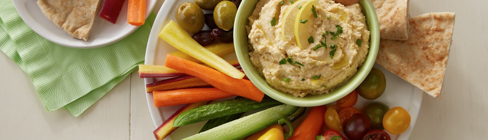 Colorful vegetables and pita chips around a bowl of hummus
