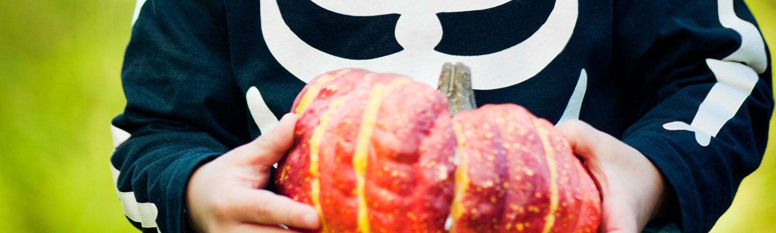 A young child in a skeleton costume holding a pumpkin