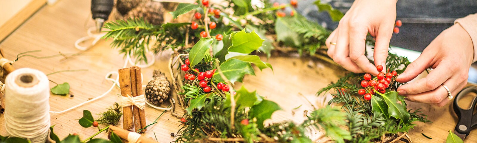 Two hands construct a holiday wreath on a wooden table