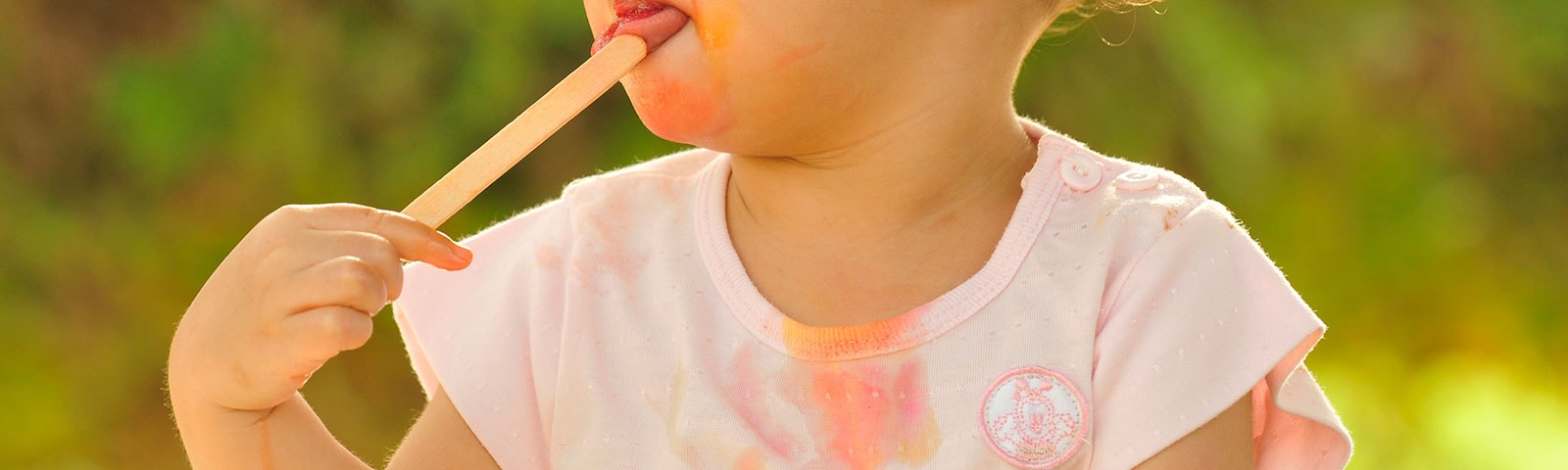 A young girl eating a melted popsicle with stains on her shirt A young girl eating a melted popsicle with stains on her shirt