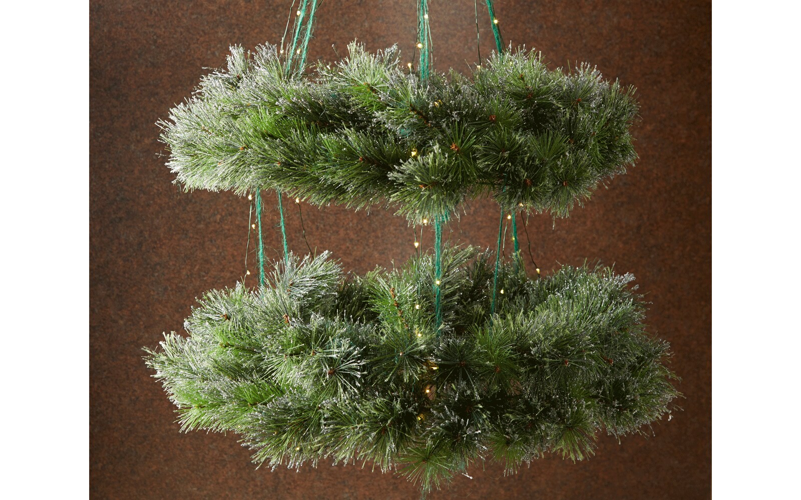 Two wreaths hanging as a chandelier by green ribbon and wrapped in Christmas lights