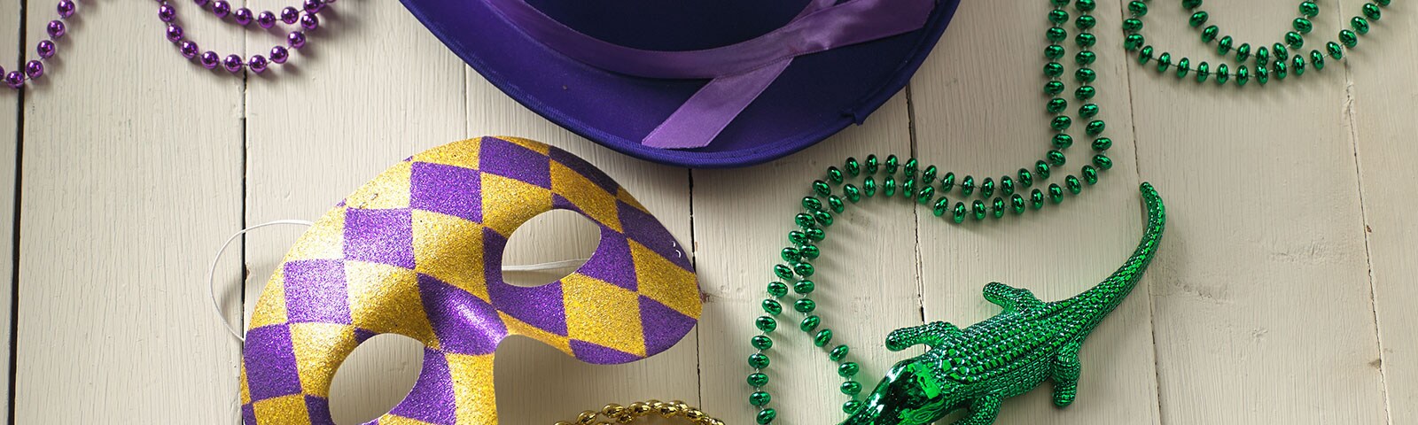 Mardi Gras beads, masks, and hats on a white painted wooden table