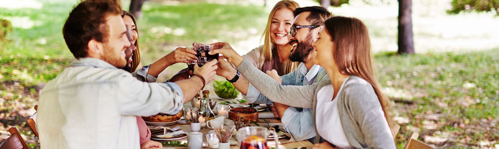 Group of friends sitting around an outdoor table sharing a friendsgiving feast and toasting one another