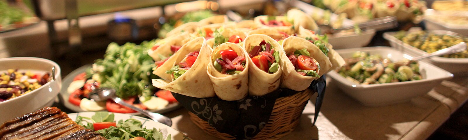 a bountiful feast of wraps, greens and pasta salads sit on a long countertop